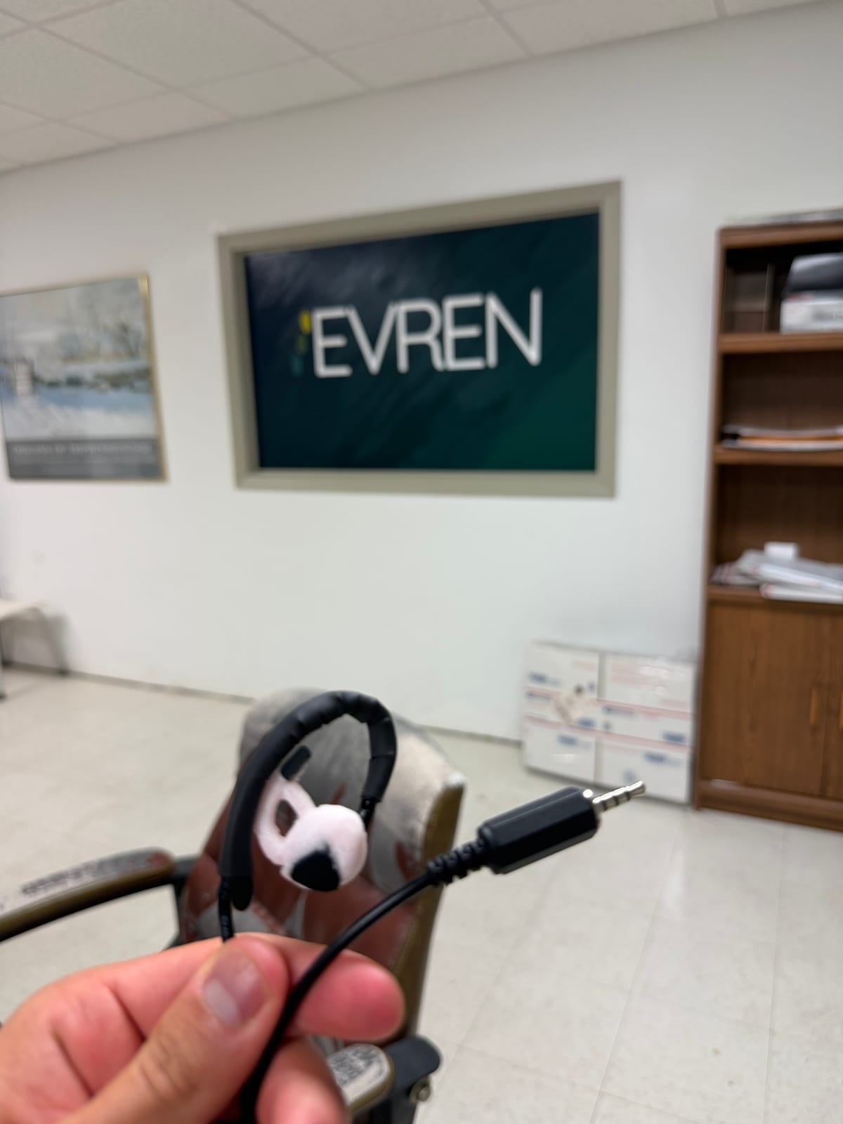 An assembled Evren ear piece held up in front of the Evren Technologies office sign